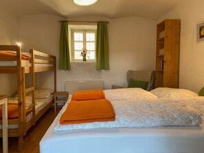 A room with bunk beds, a radiator, a window with curtains, and a wooden bookshelf.