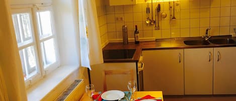 Une cuisine avec une table à manger pour deux personnes, une fenêtre avec des rideaux et un mur recouvert de carreaux.