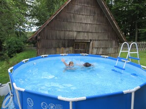 An outdoor swimming pool with a ladder, surrounded by a wooden fence and trees.