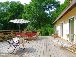 Eine Holzterrasse mit Gartenmöbeln, darunter Stühle und ein Tisch, umgeben von üppiger Vegetation.