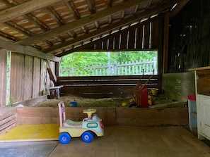 A rustic barn interior with a wooden floor, a small toy car, and a window overlooking greenery.