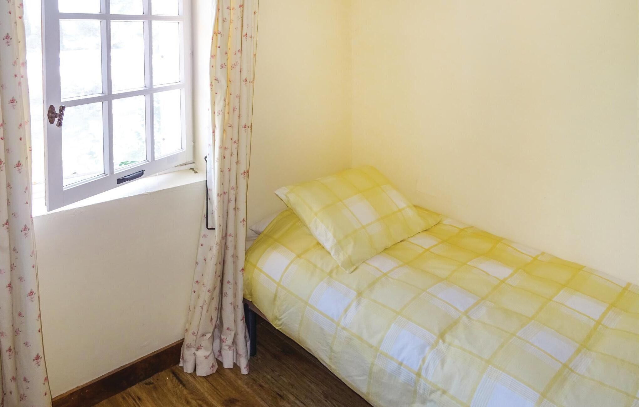Une petite chambre avec un lit simple, une fenêtre et des rideaux à motifs floraux.