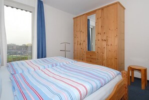 Une chambre à coucher avec un lit, une armoire en bois, une petite table en bois et une fenêtre avec des rideaux.