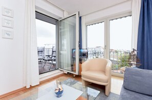 Ein modernes Wohnzimmer mit Glastür zum Balkon, einer Couch, einem Couchtisch und einem Fernseher.