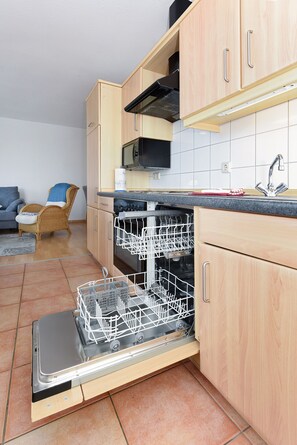 A kitchen with wooden cabinets, a dishwasher, a microwave, and a sink. - Lee - house harbor view (Esens)