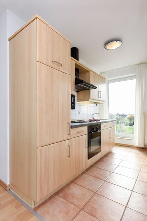 A modern kitchen with wooden cabinets, a stove, and a large window. - Lee - house harbor view (Esens)