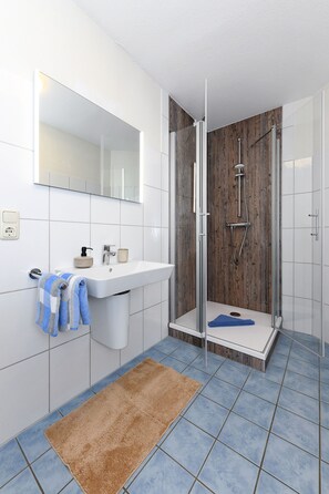 A modern bathroom with a glass-enclosed shower, a white sink, and a mirror above it. - Lee - house harbor view (Esens)