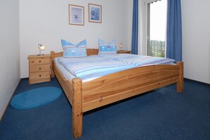 Ein Bett aus Holz mit gestreifter Bettwäsche, zwei Kissen, ein Nachttisch mit einer Lampe und ein blauer Teppich.