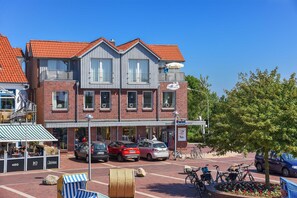 A two-story building with a red-tiled roof, a balcony, and a storefront with a sign. - Lee - house harbor view (Esens)