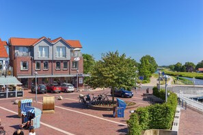 A town square with a red-brick building, bicycles, and a canal in the background. - Lee - house harbor view (Esens)