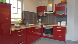 Eine Küche mit roten Schränken, einem Edelstahlbackofen, einer Kaffeemaschine und einem Toaster.