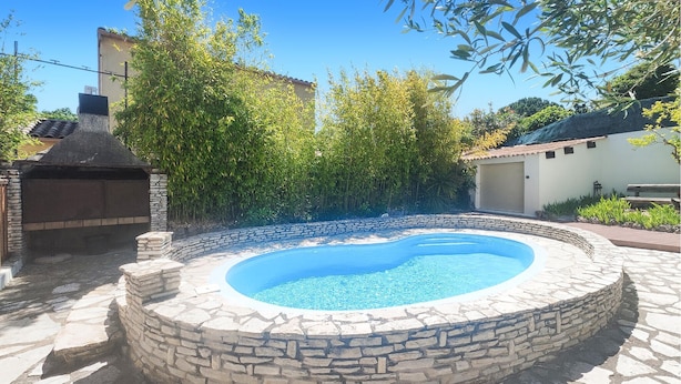 A stone pool surrounded by a stone wall, with a barbecue grill and lush greenery in the background. - Awesome home in Tourbes (Tourbes)