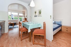 A compact room with a dining table, chairs, a bed, and a small kitchenette.