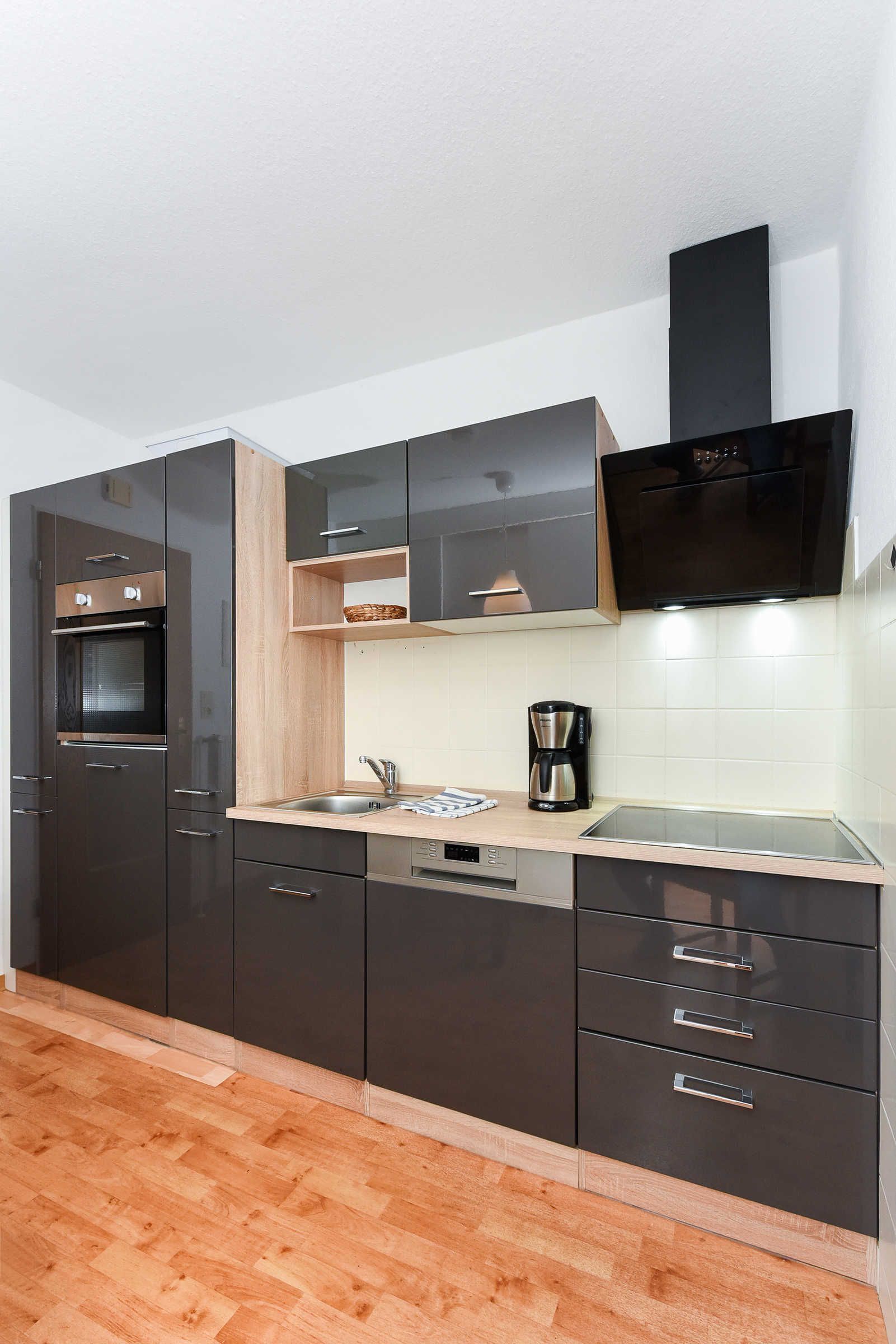 Eine moderne Küche mit dunklen Schränken, einem eingebauten Ofen, einer Mikrowelle, einer Kaffeemaschine und einer Holz Arbeitsplatte.