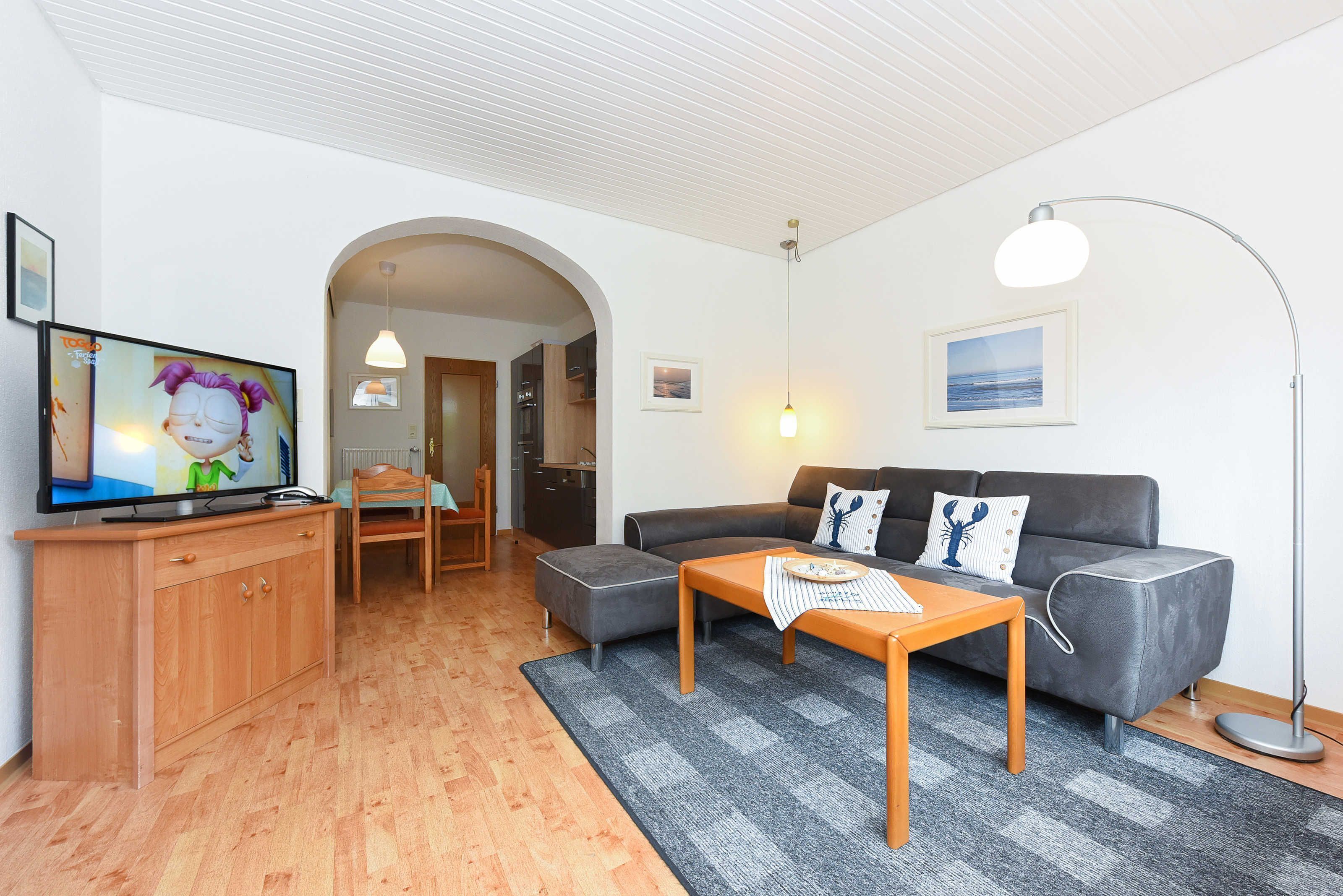 Ein modernes Wohnzimmer mit einem grauen Sofa, einem Holztisch und einem Fernseher auf einem Holzschrank.