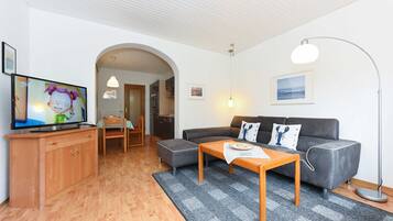 Ein modernes Wohnzimmer mit einem grauen Sofa, einem Holztisch und einem Fernseher auf einem Holzschrank.