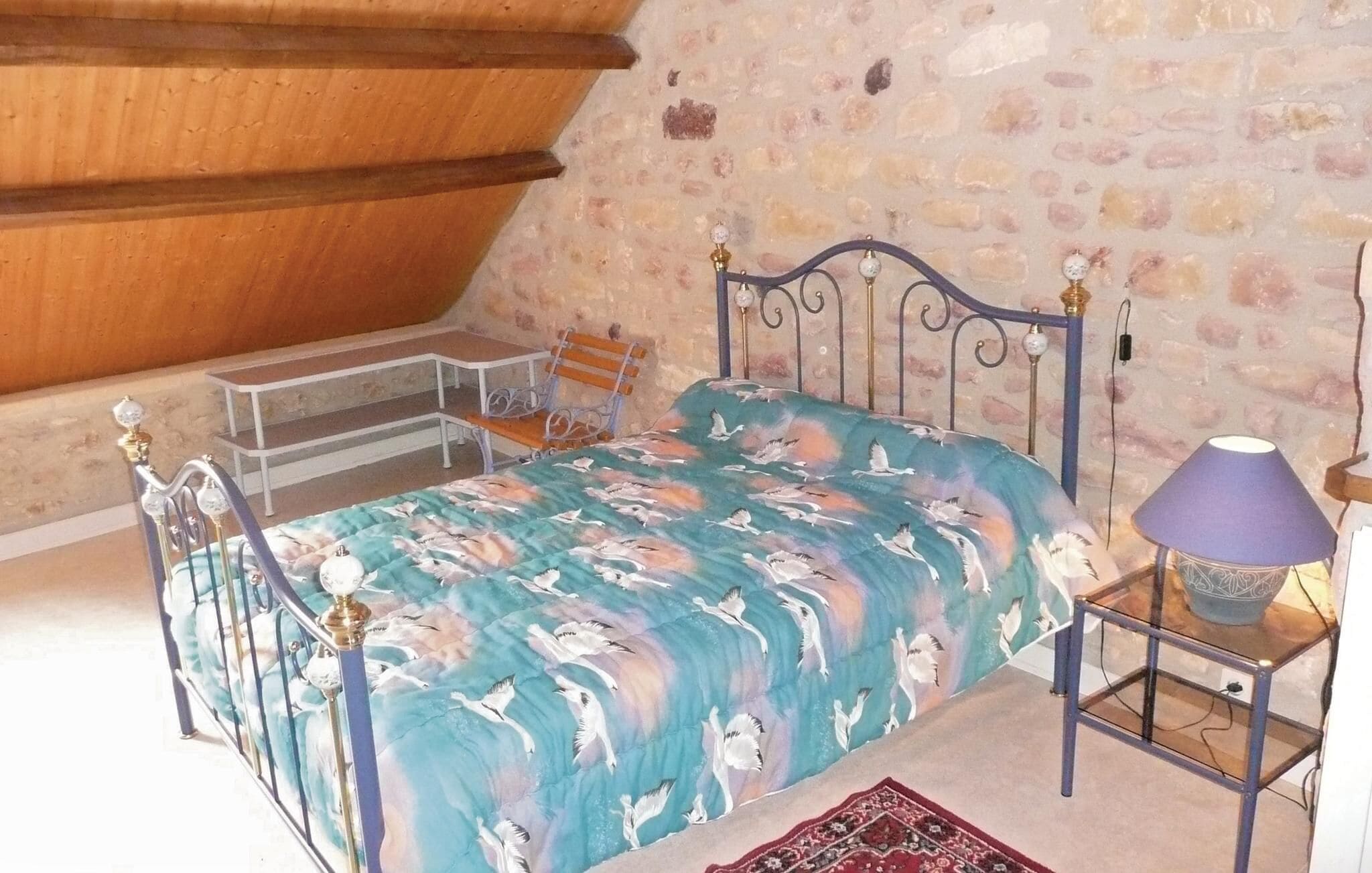 Quarto com cama, mesa de cabeceira, luminária, cadeira e uma pequena mesa.