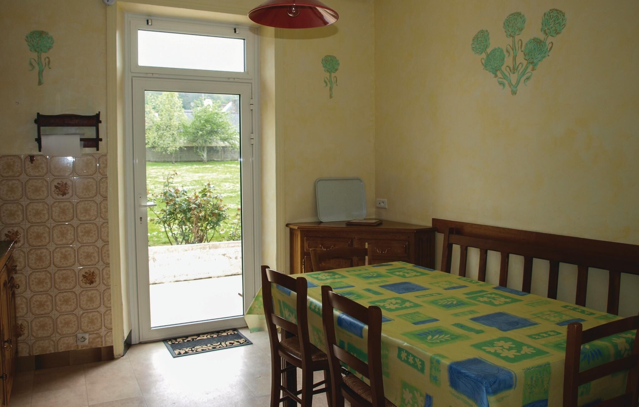 A dining area with a table and chairs, a small cabinet, and a window with a view of greenery.