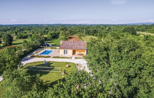 Et hus med swimmingpool, omgivet af frodig vegetation og en klar himmel.