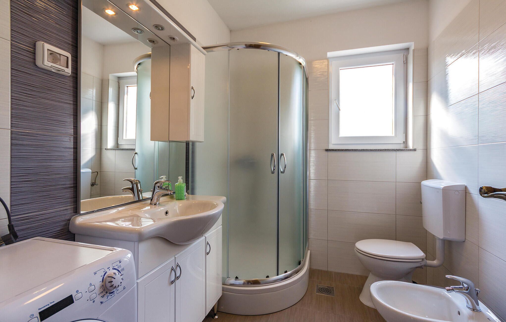 A modern bathroom with a curved shower enclosure, a sink with a mirror, and a toilet.