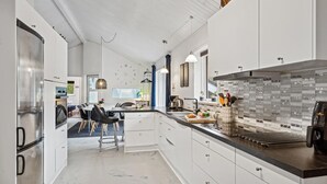 Una cocina moderna con armarios blancos, una isla central y un comedor con taburetes de bar.