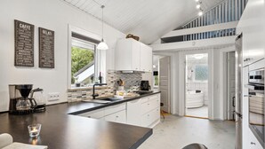 Una cocina moderna con armarios blancos, un ventanal grande y una cafetera.
