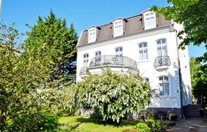 A large, white building with multiple balconies and a garden in front.