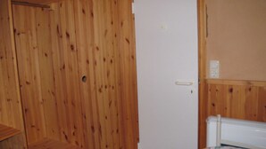 Et værelse med træpaneler, en hvid dør, en radiator og en seng med blomstret dyne.
