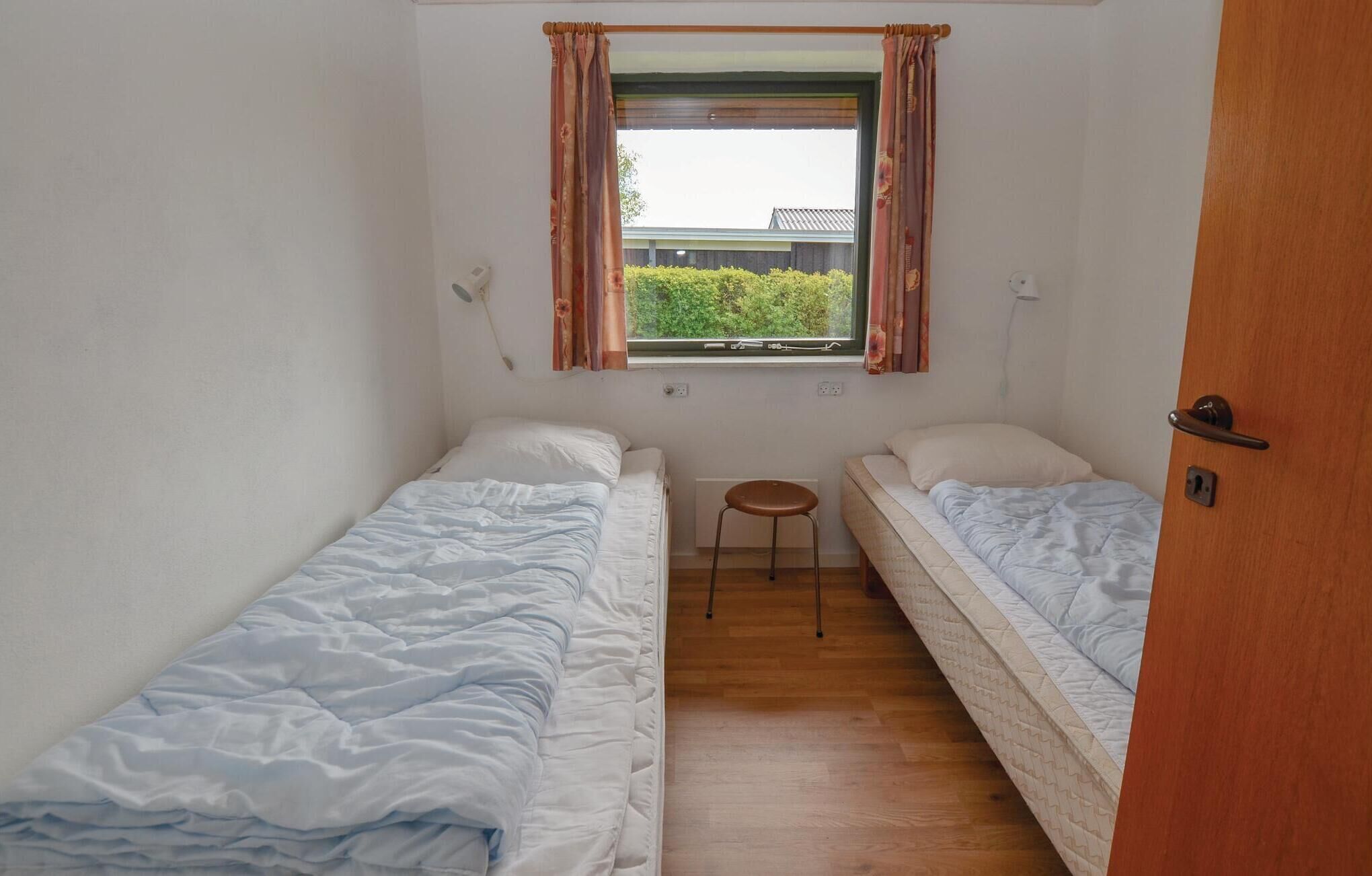 A small, single-room accommodation with two single beds, a small stool, and a window with curtains.