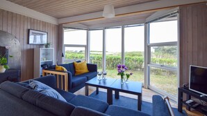 Ett modernt vardagsrum med en soffa, ett soffbord och en tv. Stora fönster ger utsikt över grönområden utanför.