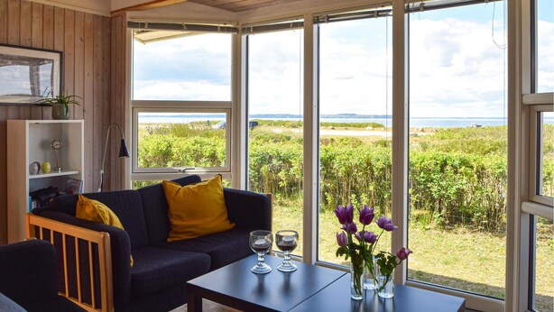 Ett rum med en mörkblå soffa, en gul kudde och ett bord med två glas och en vas med lila blommor.