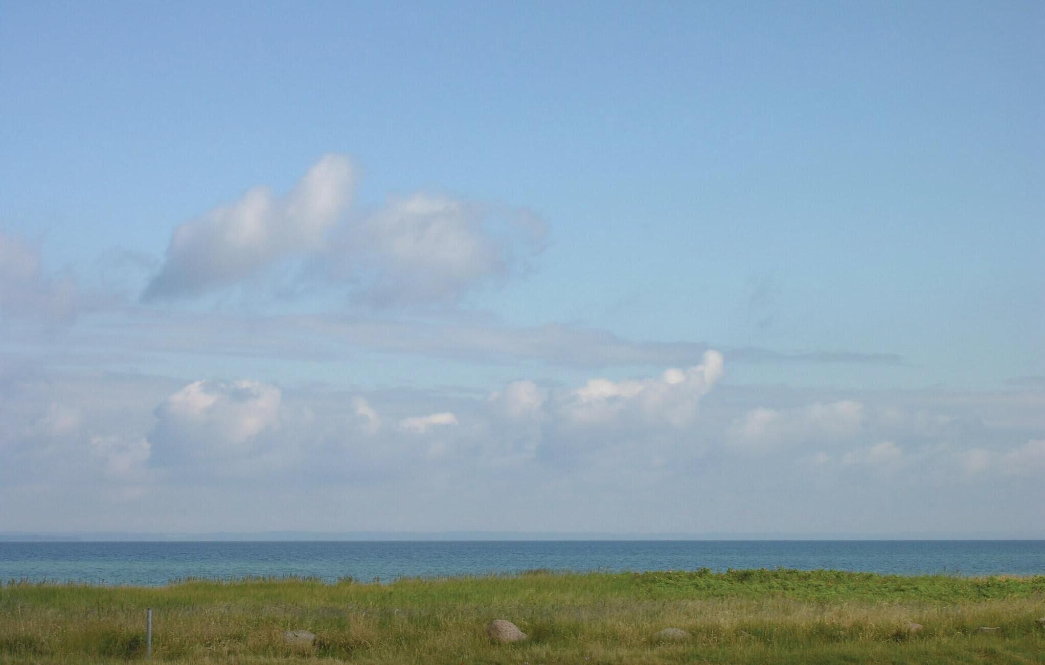A coastal landscape with a grassy foreground, a clear sky, and a calm sea.