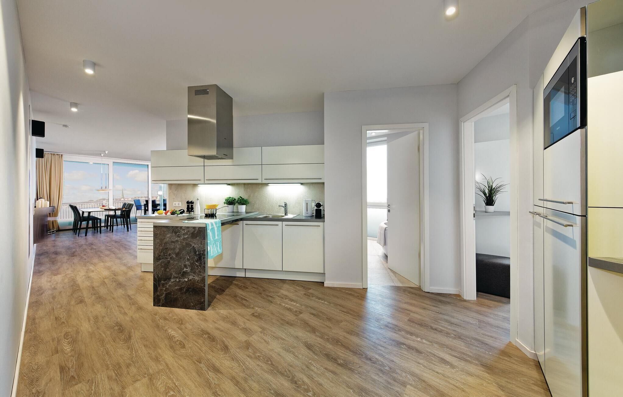 A modern kitchen with white cabinets, a marble island, and a stainless steel range hood.