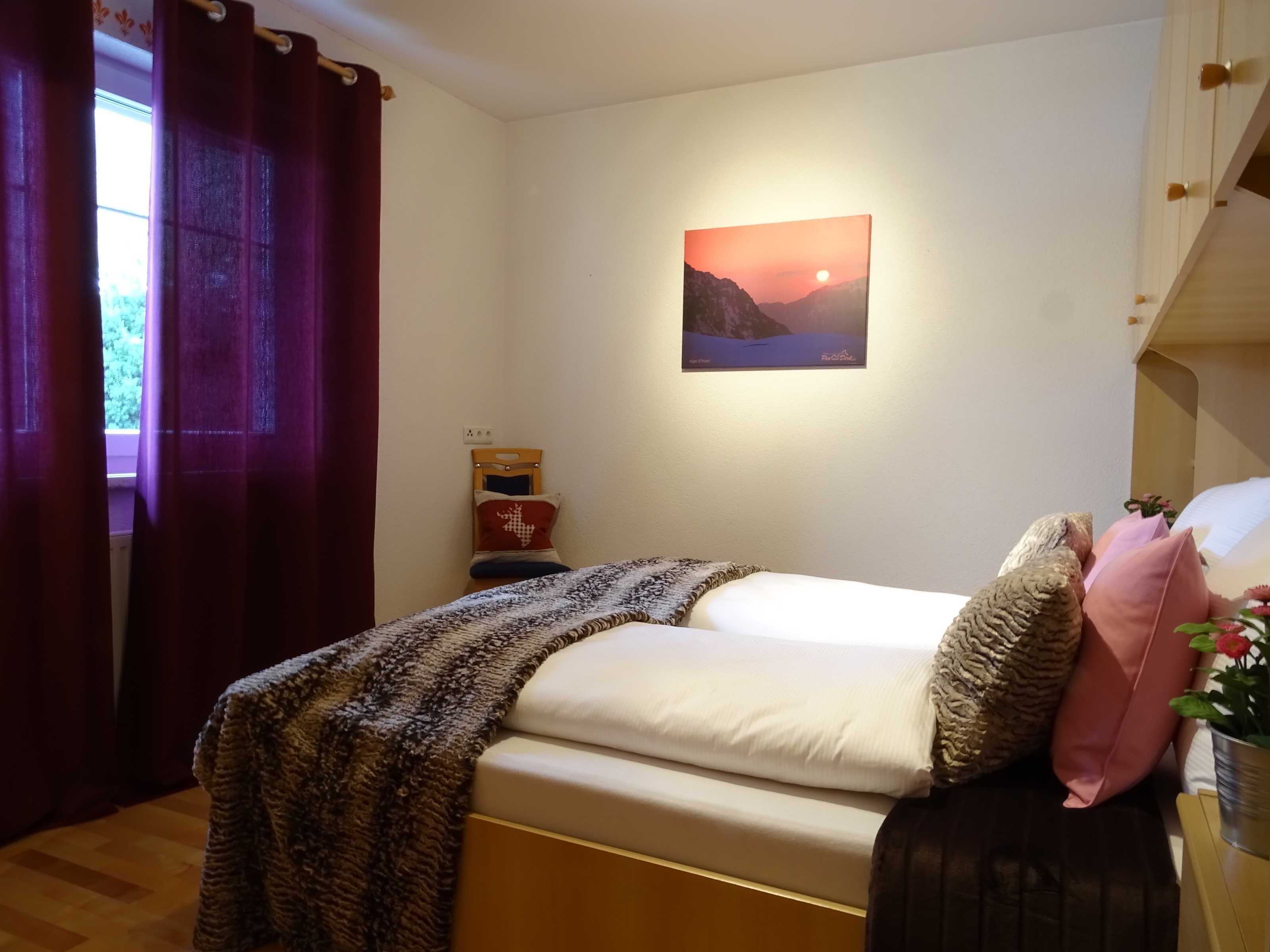 A bedroom with a bed, a nightstand, a painting, and a window with curtains.