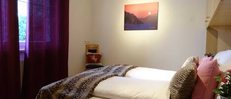 A bedroom with a bed, a nightstand, a painting, and a window with curtains.