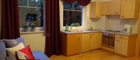 Eine kleine Küche mit Holzschränken, einem eingebauten Ofen und einem Fenster mit Vorhängen.