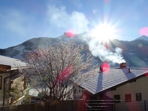 A mountain landscape with a building featuring a sloped roof and a chimney emitting smoke.