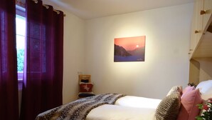 Une chambre à coucher avec un lit, une table de chevet, un tableau et une fenêtre avec des rideaux.