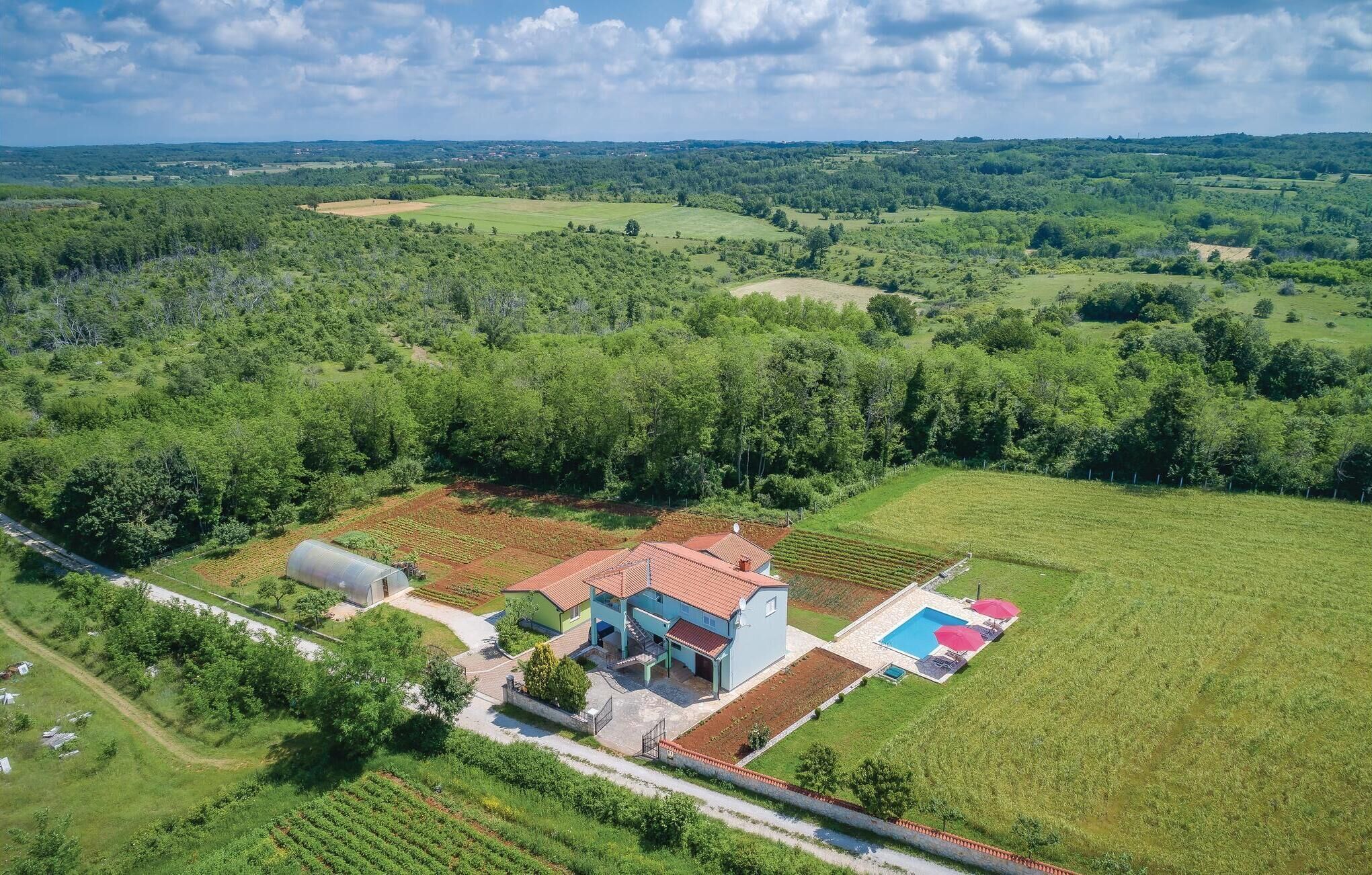 An aerial view of a property with a large house, a swimming pool, and surrounding green fields.