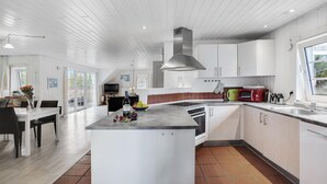 Cozinha moderna com armários brancos, uma ilha central e um espaço de refeições com mesa e cadeiras.
