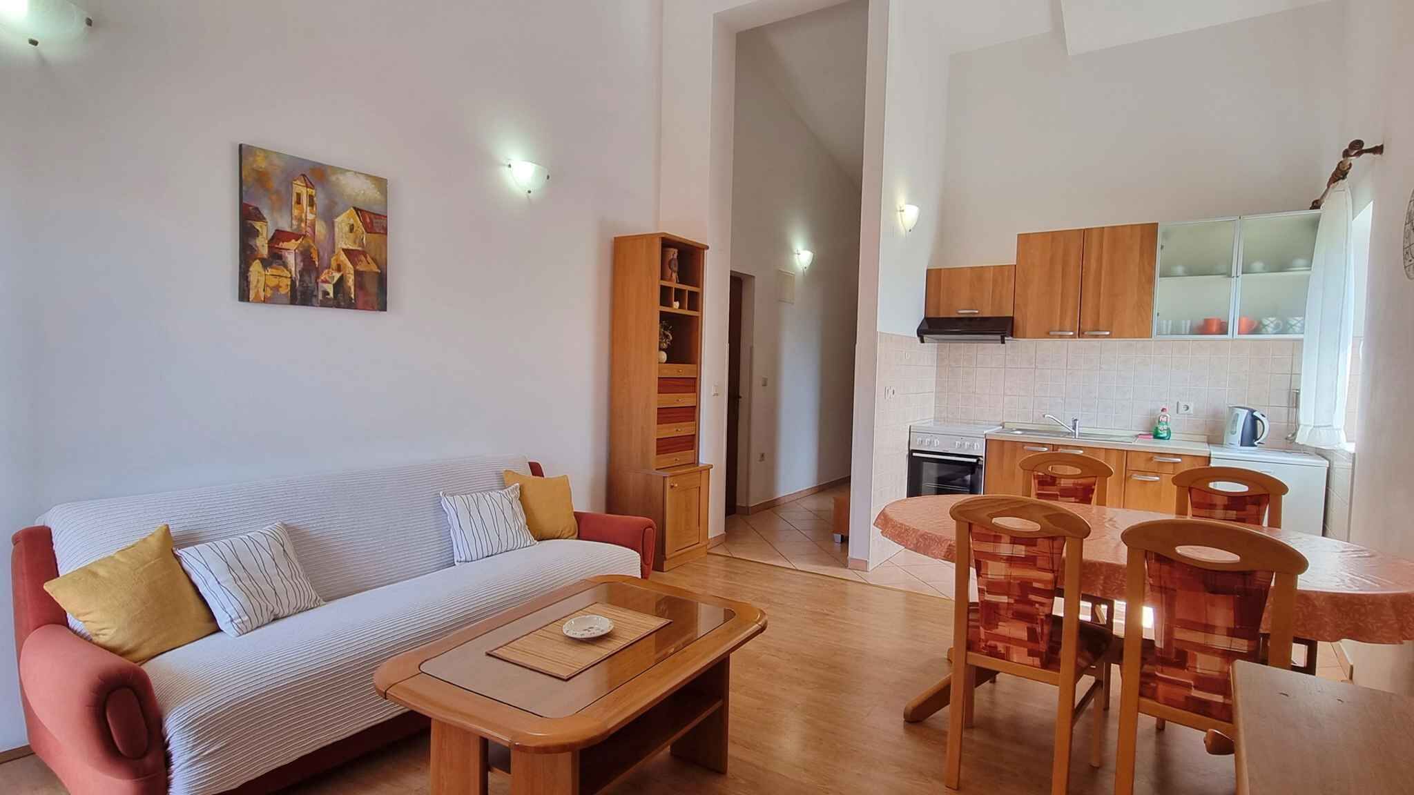 A living room with a sofa, a coffee table, and a dining area with chairs and a table. There is a kitchen with cabinets and a stove.