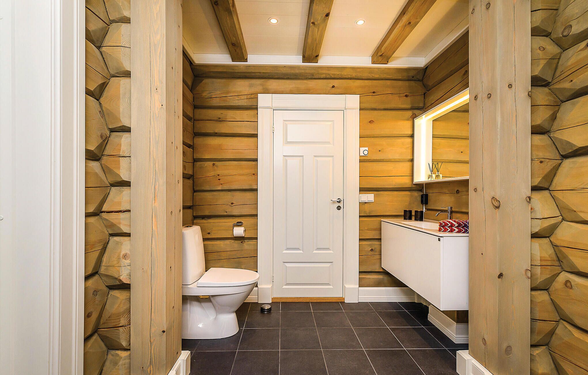 A compact bathroom with wooden walls, a white door, a toilet, a sink with a mirror, and a small countertop.