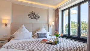 A hotel room with a bed, pillows, a bedside table, a nightstand, a window with a view, and a decorative wall piece. - Cozy apartment in Binz with WiFi (Prora/Rügen)