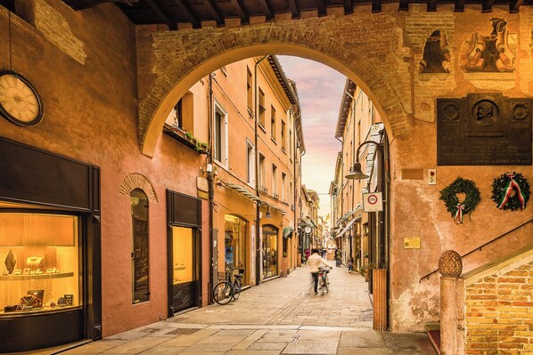 Una calle estrecha con un arco de piedra, tiendas a ambos lados y un ciclista al fondo.
