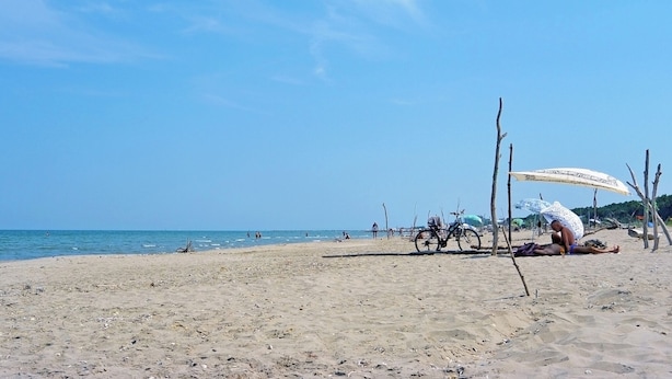 Une plage avec un ciel dégagé, un rivage sablonneux, et quelques personnes et vélos.