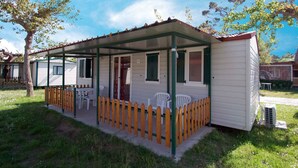 Une maison mobile d’une seule pièce, dotée d’un porche couvert, d’une porte coulissante et d’un petit espace patio avec une table et des chaises.
