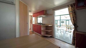 Une cuisine compacte dotée d’un plan de travail en bois, de placards rouges et d’une porte-fenêtre coulissante donnant sur un espace repas extérieur.
