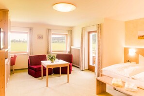 Ett hotellrum med en säng, en röd soffa, ett träbord och ett fönster med gardiner.