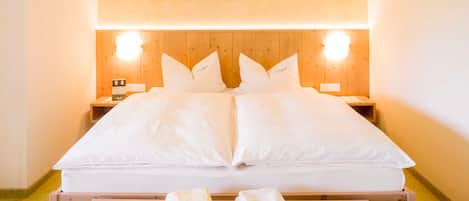 A neatly made bed with white linens, two bedside tables, and a wooden nightstand.