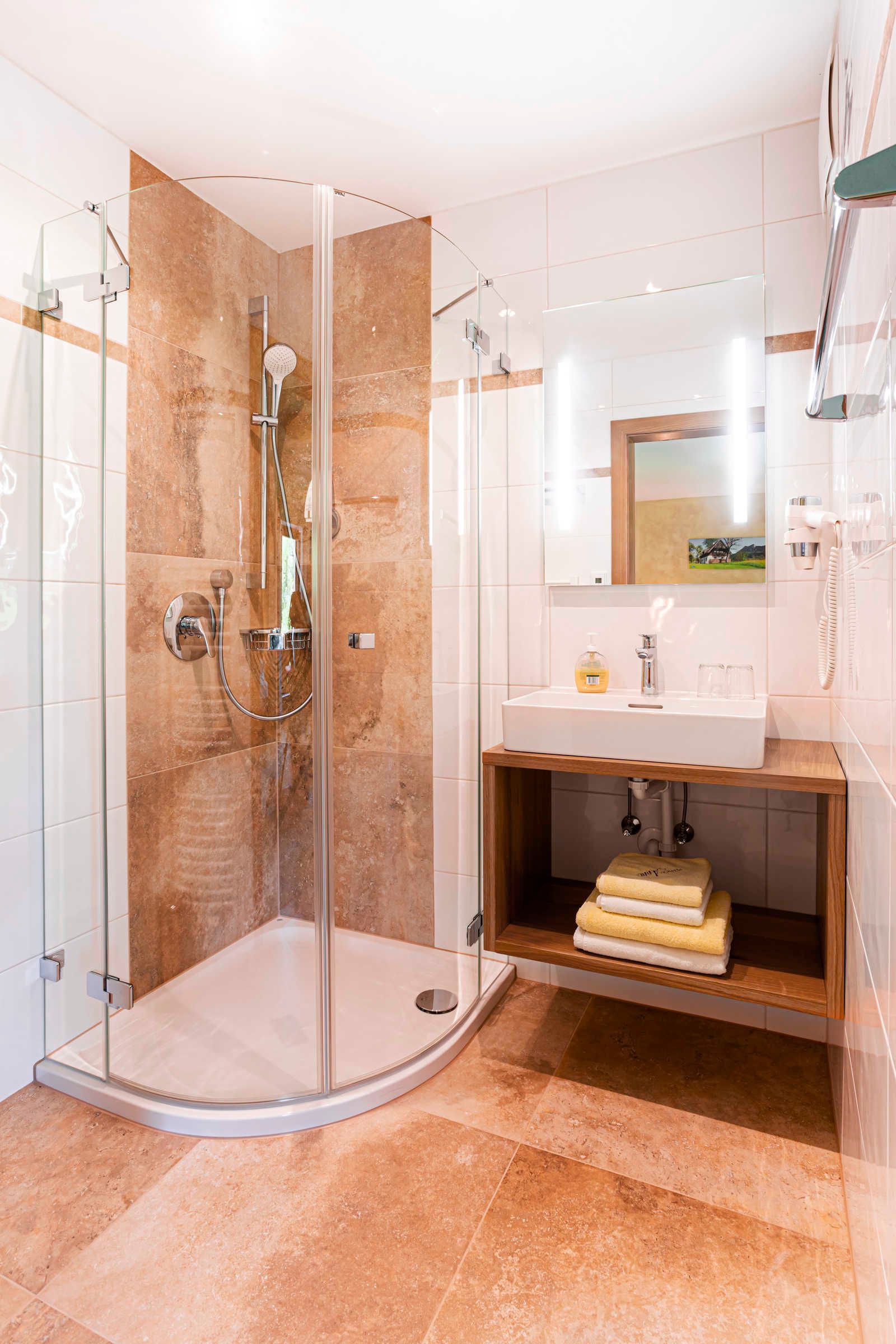 A modern bathroom with a glass-enclosed shower, a sink with a mirror above, and a wooden shelf with towels.
